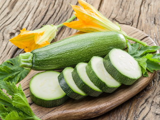 Zucchini with slices and zucchini flowers on a wooden table.