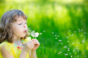Happy child blowing dandelion flower outdoors