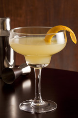Alcohol cocktail glass with lemon peel on the brown table.