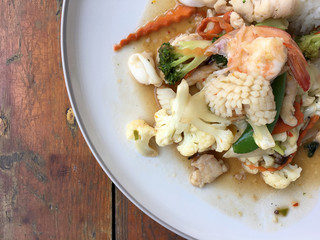 Mix of fried vegetables, Cauliflower, Carrot, Sugar Pea with seafood with rice and fried egg in white plate on wooden background. Thai style food.