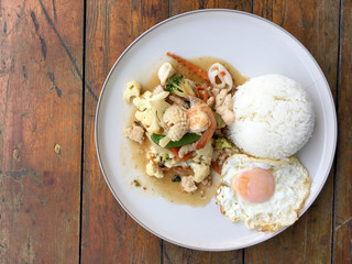 Mix of fried vegetables, Cauliflower, Carrot, Sugar Pea with seafood with rice and fried egg in white plate on wooden background. Thai style food.