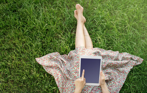 Woman relaxing on green grass and using tablet in Spring or summer time, Top view, Tablet screen is clipping path