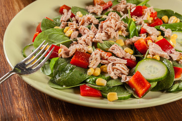 Fresh spinach salad with tuna, cucumber, corn, and red paprika on a plate