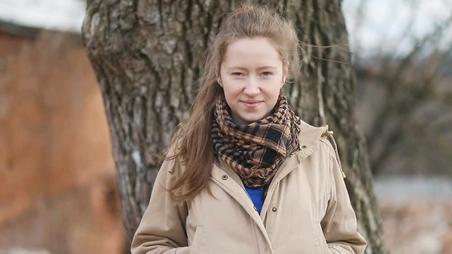 Young pretty beatiful woman in beige caot and checkered scarf walking, winking and looking in the camera, Steady cam, slow mo shot