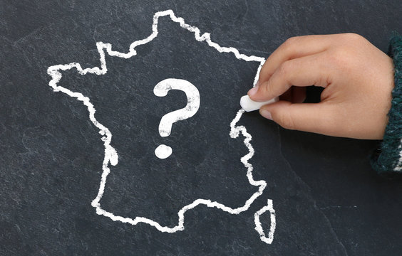 Enfant dessinant la carte de France avec un point d'interrogation sur une ardoise