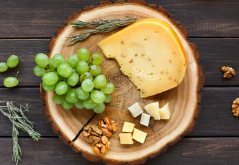 Cheese platter, gouda herb on natural wood disc with grapes and nuts - obrazy, fototapety, plakaty
