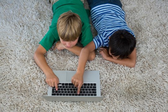 Siblings lying on rug and using laptop in living room