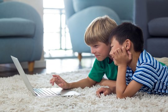 Siblings lying on rug and using laptop in living room