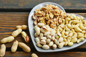 4 different types of nuts.
Cashews,Peanuts,Pistachios and Walnuts in shape-heart bowl on wooden floor.