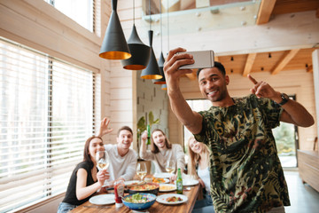 Cheerful man taking selfie with his friends at the table