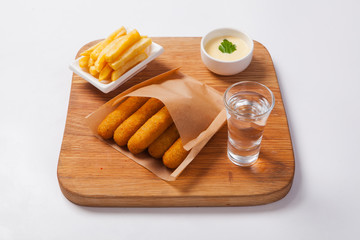 Fish sticks on a wooden board with sauce and fried potatoes