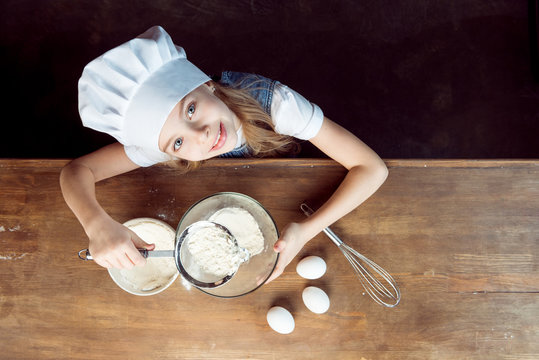 Overhead View Of Girl Making Dough For Cookies On Wooden Table