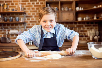 Fototapeta na wymiar little boy making pizza dough on wooden tabletop in kitchen