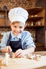 little boy in chef hat cutting mushrooms for pizza ingredients