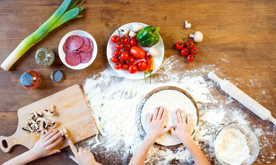 top view of children making pizza dough and preparing pizza ingredients in kitchen