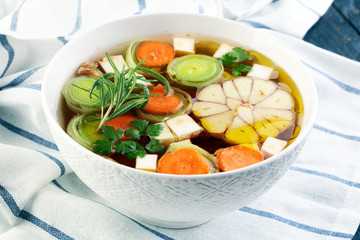 Broth with carrots, onions various fresh vegetables in a pot - colorful fresh clear spring soup. Rural kitchen scenery vegetarian bouillon or stock