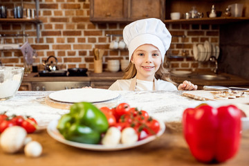 portrait of little girl with pizza dough and various ingredients
