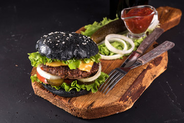 Fresh homemade burger on wooden serving board with fork and knife tomato sauce on dark background