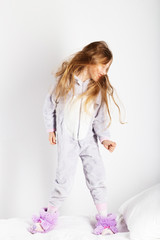 Naklejka premium Funny little girl in pajamas jumping and having fun in bed at home.