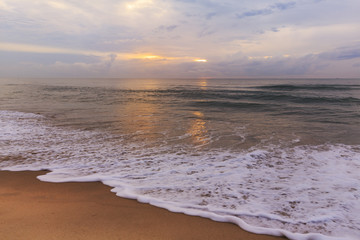 Obraz premium soft ocean waves breaking on sandy beach at early morning beach with the sun rising from the horizon