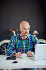 Caucasian businessman using laptop computer and drinking coffee while sitting and working in home office.