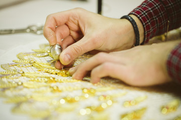 Detail of a man's hands embroiderer with a sewing thread gold on fabric.