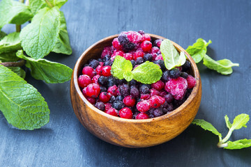 Frozen berries in wooden bowl with blueberries, raspberries, balck and red currants and mint