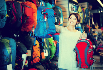 smiling female shopper examining rucksacks in sports equipment store