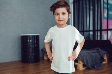 Little smiling boy in white t-shirt standing on loft studio background. Mock up.