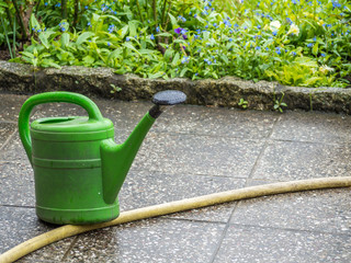 Grüne Gießkanne mit Gartenschlauch