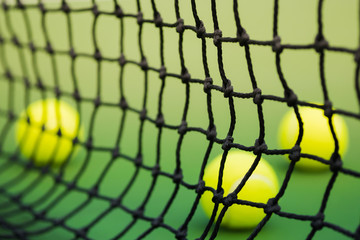 net of tennis in green court, three balls in background, blurred