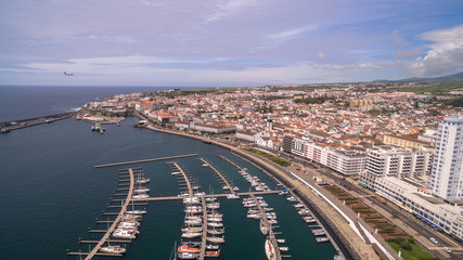 Fototapeta premium A view on Ponta Delgada from marina, Sao Miguel, Azores, Portugal. Moored yachts and boats along the port piers on a beautiful morning.