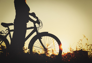 Fototapeta na wymiar silhouette of young woman riding bike at sunset