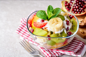 Fresh fruit salad with yogurt and walnuts in glass bowl on stone background.