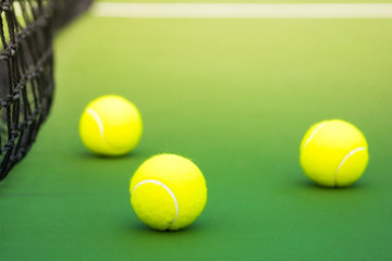 three tennis balls on green hard court with part of black weaved net