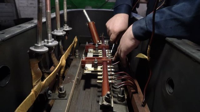 Worker twists the terminals of industrial transformer.