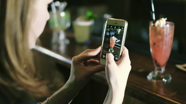 Beautiful woman taking pictures of a cocktail at the bar 4k