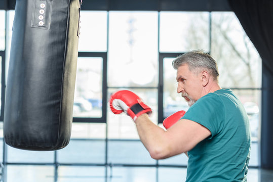 senior sportsman in red boxing gloves punching bag in fitness class