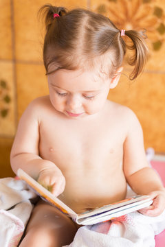 After bath.Cute little girl after bath feeling fresh and reading from a picture book