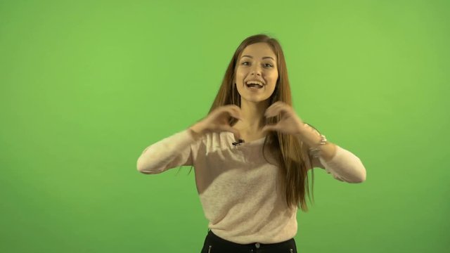 Beautiful young white model on a green screen background. Smiles, shows a gesture of love and good-bye.