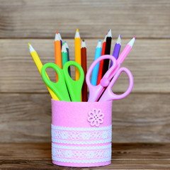 Colored pencils and scissors in a decorative jar. Recycled metal jar for storage of stationery isolated on wooden background. Closeup