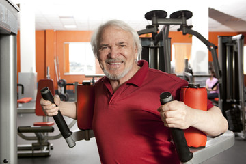 Attractive elderly man using rotary torso trainer in gym