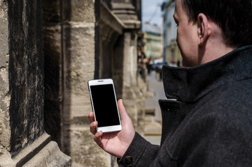 close up white mobile phone holding young hipster business man on the background of stone wall of the old city