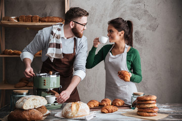 Cheerful loving couple bakers drinking coffee. Looking aside.