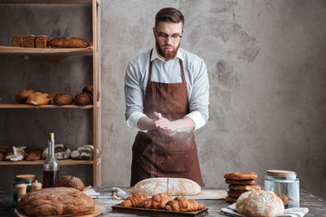 Young concentrated bearded man wearing glasses baker