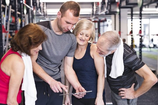 Group of fit seniors and personal trainer in gym looking at tablet