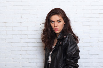 Young Beautiful Brunette Girl Wearing Leather Jacket Closeup Side View Over White Brick Wall Background