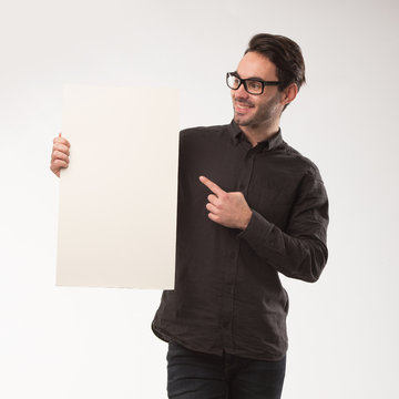 Young happy man showing presentation, pointing on placard over gray background