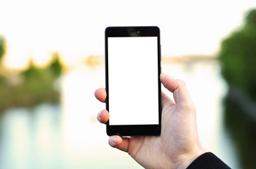 Photo of a man's hand holding black phone with blank screen with blurred lake or river in the background