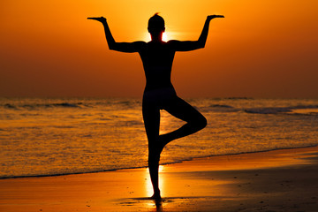 Fototapeta Kobieta ćwicząca jogę na plaży przy zachodzie słońca obraz